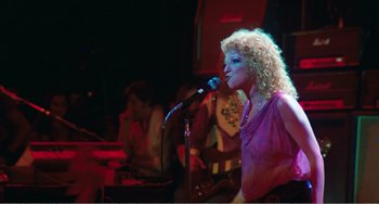 Movie still from “The Rose” (1979), directed by Mark Rydell – A woman with curly blonde hair singing into a microphone; Medium shot, Low angle