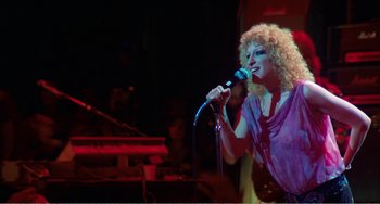 Movie still from “The Rose” (1979), directed by Mark Rydell – A woman with curly blonde hair singing into a microphone; Medium shot, Low angle