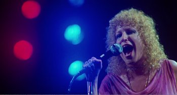 Movie still from “The Rose” (1979), directed by Mark Rydell – A woman with curly blonde hair singing into a microphone; Close Up shot, Low angle