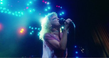 Movie still from “The Rose” (1979), directed by Mark Rydell – A woman with curly blonde hair singing into a microphone; Medium shot, Low angle