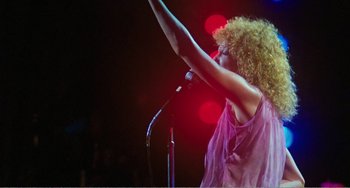 Movie still from “The Rose” (1979), directed by Mark Rydell – A woman with curly hair is holding a microphone; Medium shot, Low angle