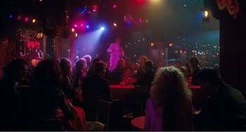 Movie still from “The Rose” (1979), directed by Mark Rydell – A crowd of people sitting at tables in front of a microphone; Wide shot, Over the shoulder angle