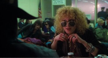 Movie still from “The Rose” (1979), directed by Mark Rydell – A woman sitting at a table in front of a group of people; Medium shot, Over the shoulder angle
