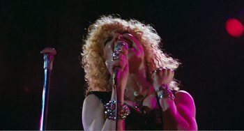 Movie still from “The Rose” (1979), directed by Mark Rydell – A woman with curly blonde hair singing into a microphone; Medium shot, Low angle