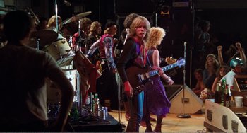 Movie still from “The Rose” (1979), directed by Mark Rydell – A group of people that are standing around a stage; Wide shot, Low angle