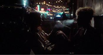 Movie still from “The Rose” (1979), directed by Mark Rydell – Two people sitting in a car at night with lights in the background; Wide shot, Over the shoulder angle