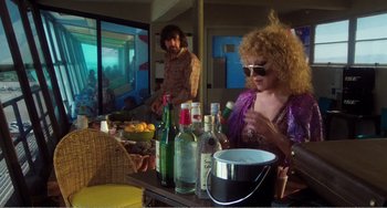 Movie still from “The Rose” (1979), directed by Mark Rydell – A man and a woman sitting at a table with bottles of alcohol; Medium shot, High angle