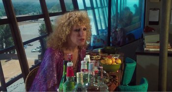 Movie still from “The Rose” (1979), directed by Mark Rydell – A woman sitting in front of a table filled with drinks; Medium shot, High angle