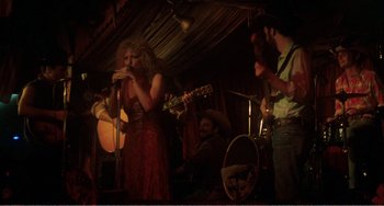Movie still from “The Rose” (1979), directed by Mark Rydell – A group of people singing and playing instruments in a room; Wide shot, Low angle
