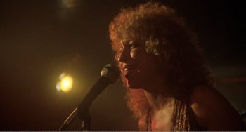 Movie still from “The Rose” (1979), directed by Mark Rydell – A woman with curly hair is singing into a microphone; Close Up shot, Low angle