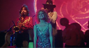 Movie still from “The Rose” (1979), directed by Mark Rydell – A woman in a silver sequined dress is standing on a stage; Medium shot, Low angle