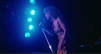 Movie still from “The Rose” (1979), directed by Mark Rydell – A woman in a red sequined dress holding a microphone; Medium shot, Low angle