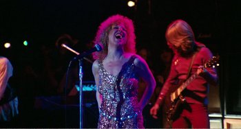 Movie still from “The Rose” (1979), directed by Mark Rydell – A woman singing into a microphone on a stage; Medium shot, Low angle