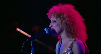 Movie still from “The Rose” (1979), directed by Mark Rydell – A woman with curly red hair singing into a microphone; Close Up shot, Low angle