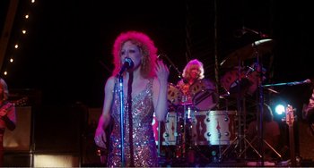 Movie still from “The Rose” (1979), directed by Mark Rydell – A woman singing into a microphone on a stage; Medium shot, Low angle