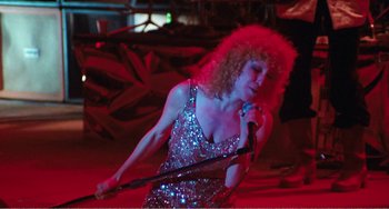 Movie still from “The Rose” (1979), directed by Mark Rydell – A woman with curly hair is holding a microphone; Medium shot, Low angle