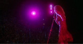 Movie still from “The Rose” (1979), directed by Mark Rydell – A woman in a red dress holding a red microphone; Wide shot, Low angle