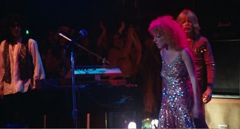 Movie still from “The Rose” (1979), directed by Mark Rydell – A woman with pink curly hair standing in front of a microphone; Medium shot, Low angle