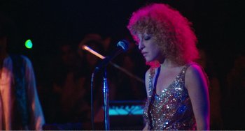 Movie still from “The Rose” (1979), directed by Mark Rydell – A woman with curly red hair standing in front of a microphone; Medium shot, Low angle