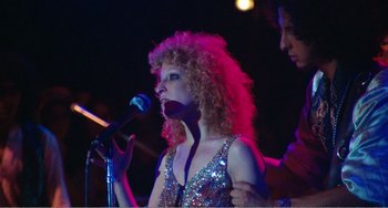 Movie still from “The Rose” (1979), directed by Mark Rydell – A woman with curly red hair singing into a microphone; Medium shot, Low angle