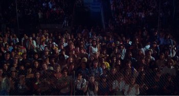 Movie still from “The Rose” (1979), directed by Mark Rydell – A crowd of people sitting and standing in front of a fence; Extreme Wide shot, High angle