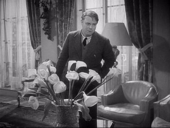 Movie still from “The Rules of the Game” (1939), directed by Jean Renoir – A black and white photo of a man standing in front of a vase of flowers; Medium shot, Over the shoulder angle
