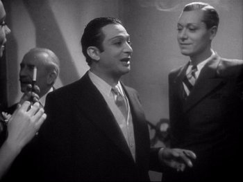 Movie still from “The Rules of the Game” (1939), directed by Jean Renoir – A man in a suit and tie standing next to two other men; Medium shot, Over the shoulder angle