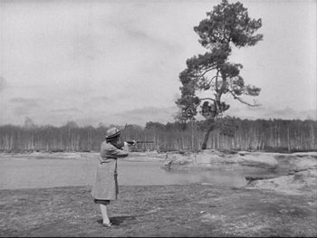 Movie still from “The Rules of the Game” (1939), directed by Jean Renoir – An old black and white photo of a woman holding a gun; Wide shot, Low angle