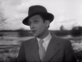 Movie still from “The Rules of the Game” (1939), directed by Jean Renoir – A black and white photo of a man wearing a suit and a hat; Close Up shot, Over the shoulder angle