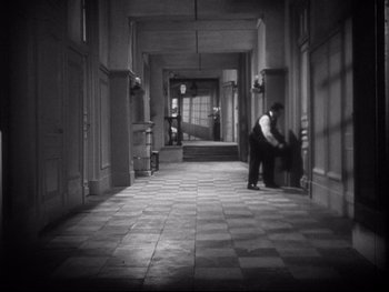 Movie still from “The Rules of the Game” (1939), directed by Jean Renoir – A man in a black shirt and a white shirt is in a hallway; Extreme Wide shot, High angle
