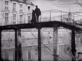 Movie still from “The Rules of the Game” (1939), directed by Jean Renoir – Two people standing on a bridge over a river; Wide shot, Low angle