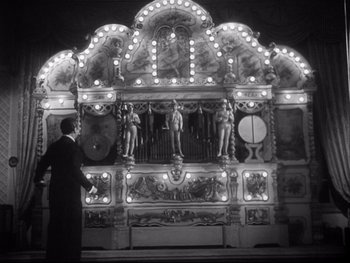 Movie still from “The Rules of the Game” (1939), directed by Jean Renoir – A black and white photo of a man standing in front of an organ; Wide shot, Low angle