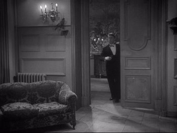 Movie still from “The Rules of the Game” (1939), directed by Jean Renoir – A black and white photo of a man in a tuxedo in front of an open door; Wide shot, High angle