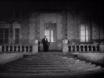 Movie still from “The Rules of the Game” (1939), directed by Jean Renoir – A man standing in front of an entrance to a building; Extreme Wide shot, Over the shoulder angle