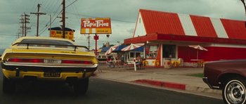 Movie still from “The Runaways” (2010), directed by Floria Sigismondi – A car driving down a street next to a restaurant; Wide shot, Low angle