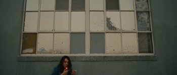 Movie still from “The Runaways” (2010), directed by Floria Sigismondi – A woman sitting in front of a building holding a cigarette; Medium shot, Low angle