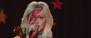 Movie still from “The Runaways” (2010), directed by Floria Sigismondi – A woman with a painted face is singing into a microphone; Close Up shot, Over the shoulder angle