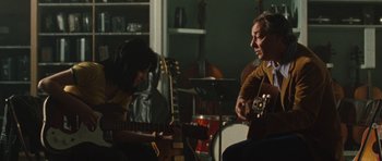 Movie still from “The Runaways” (2010), directed by Floria Sigismondi – A man and a woman are playing a guitar together; Medium shot, Over the shoulder angle