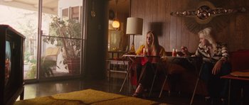 Movie still from “The Runaways” (2010), directed by Floria Sigismondi – A woman sitting at a table in a living room; Wide shot, Low angle