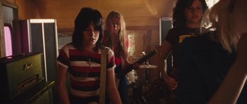 Movie still from “The Runaways” (2010), directed by Floria Sigismondi – A group of people that are in a room with instruments; Medium shot, Low angle
