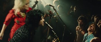 Movie still from “The Runaways” (2010), directed by Floria Sigismondi – A group of people singing into microphones in a dark room; Medium shot, Overhead angle