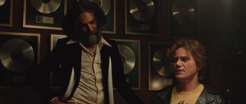 Movie still from “The Runaways” (2010), directed by Floria Sigismondi – A man with long hair and a beard standing next to a woman; Medium shot, Over the shoulder angle