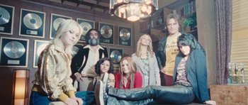 Movie still from “The Runaways” (2010), directed by Floria Sigismondi – A group of people standing in a room with many records on the wall behind them; Wide shot, Low angle