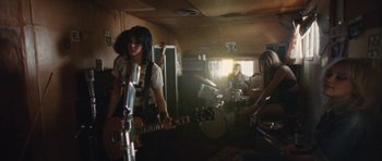 Movie still from “The Runaways” (2010), directed by Floria Sigismondi – A group of young people in a room with a guitar; Wide shot, Low angle