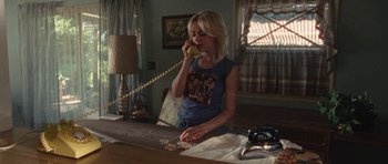 Movie still from “The Runaways” (2010), directed by Floria Sigismondi – A woman sitting at a table talking on the phone; Medium shot, High angle