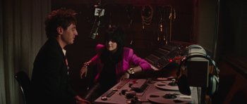 Movie still from “The Runaways” (2010), directed by Floria Sigismondi – A woman in a pink jacket sitting next to a man in a purple jacket; Medium shot, Low angle