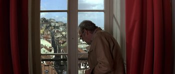 Movie still from “The Russia House” (1990), directed by Fred Schepisi – An older man standing in front of a window looking out at a city; Medium shot, High angle