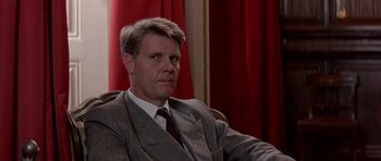 Movie still from “The Russia House” (1990), directed by Fred Schepisi – A man wearing a suit and tie sitting in a chair; Close Up shot, Low angle