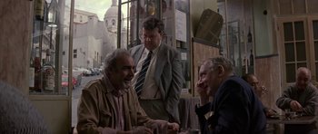 Movie still from “The Russia House” (1990), directed by Fred Schepisi – A group of men sitting at a table outside; Medium shot, Over the shoulder angle