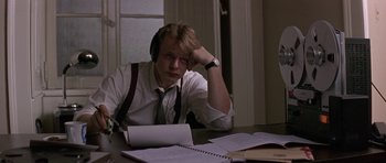 Movie still from “The Russia House” (1990), directed by Fred Schepisi – A man sitting at a table wearing headphones; Medium shot, High angle